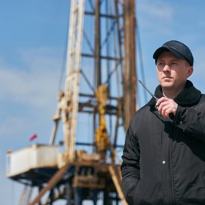 Security guard using portable wireless transceiver. Security man with walkie talkie, standing outdors against oil drilling station platform, safety concept